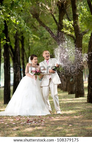 Newly married couple, very happiness and fun, open champagne outdoor in sunny day. Focus on bottle champagne.