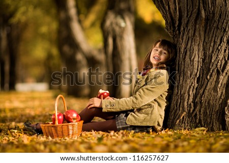 happy beautiful little girl sit on autumnal  leaf and eat apple