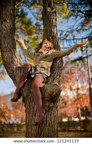 vertical photo,  happy beautiful little girl sit on tree and joyful  laughter , in autumnal park