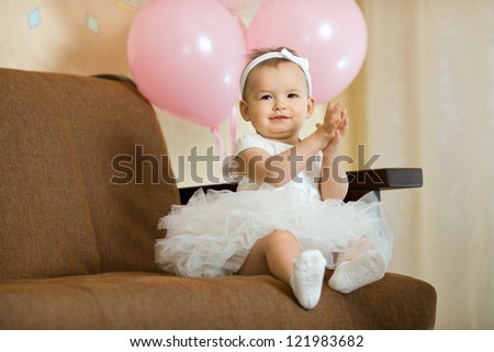 the happy little baby girl in white dress smile , sit on sofa indoor