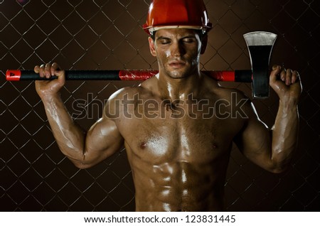 the muscular  tired worker chopper man, in  safety helmet  with big  heavy ax  in hands, on netting fence background