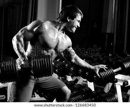 very power athletic guy ,  execute  traction with  dumbbells, exercise on broadest muscle of back, in sport hall,  black-and-white photo