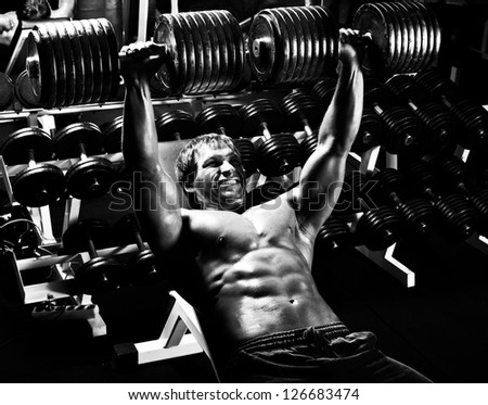 very power athletic guy ,  execute exercise press with  dumbbells, in sport hall,  black-and-white photo