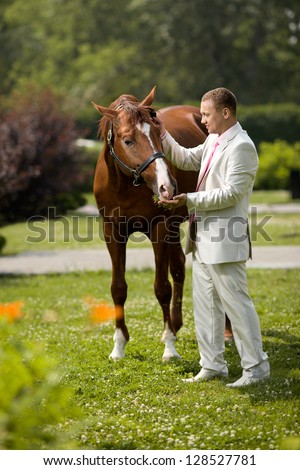man bridegroom in white nuptial dress, stand with beautiful big horse on nature, summer sunny day