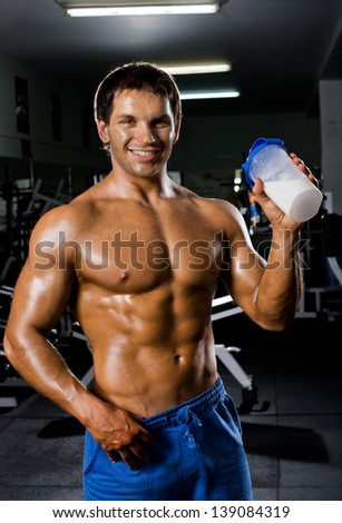 the very muscular sporty  guy drinking  protein in dark weight room, naked  torso