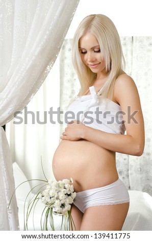 happy young pregnant woman in white dress, in  light bedroom