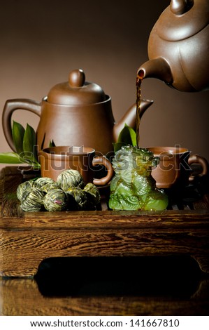 vertical photo, of the clay teapot tea flow in  cup on brown background,  tea ceremony