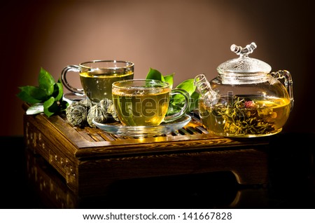 horizontal  photo  of the glass teapot with green tea in cup, on  on brown backgrpund, closeup