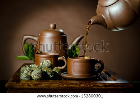 horizontal photo, of the clay teapot tea flow in  cup on brown background,  tea ceremony