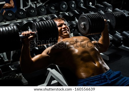 very power athletic guy ,  execute exercise press with  dumbbells, in sport hall