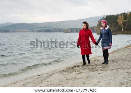 beauty mature woman in red topcoat with young daughter, walking outdoor on water moorage for boat, in autumn cold overcast day