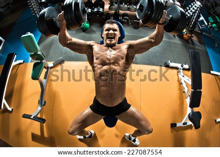 very power athletic guy bodybuilder ,  execute exercise press of dumbbells on pectoral muscle, in gym