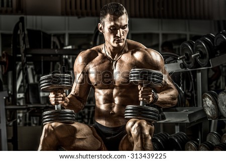 very power athletic guy bodybuilder , sit with  dumbbells, in dark gym