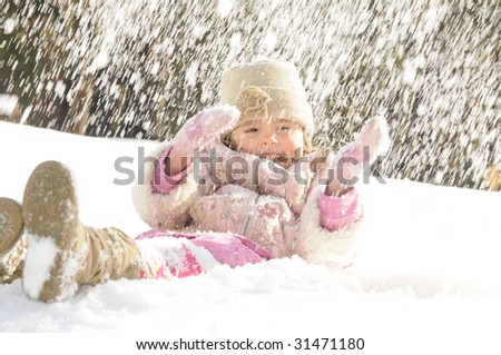 The little girl lays on a snow, on her throw a snow in the winter