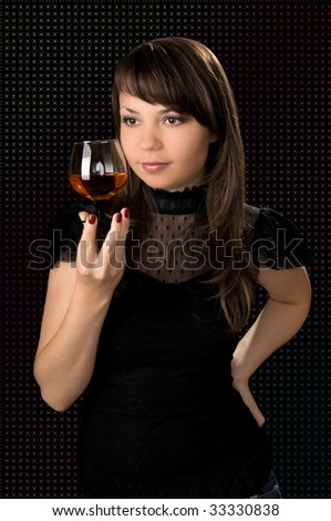 Young beautiful  the woman holds in one hand a glass with an alcoholic drink on black background