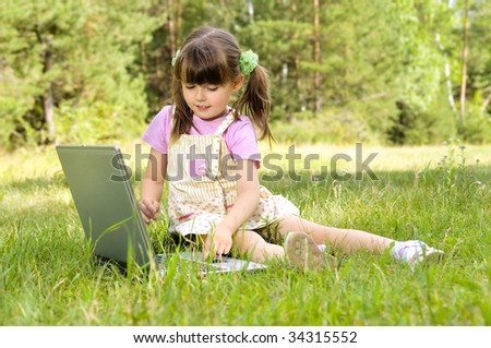 The small nice girl works on a computer, sits on a beautiful green lawn