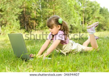 The small nice girl works on a computer, lays on a beautiful green lawn, Smile .