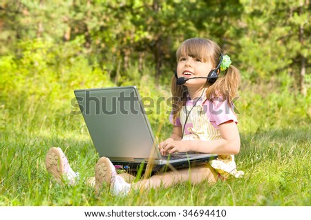 The small nice girl works on a computer, lays on a beautiful green lawn, Smile .