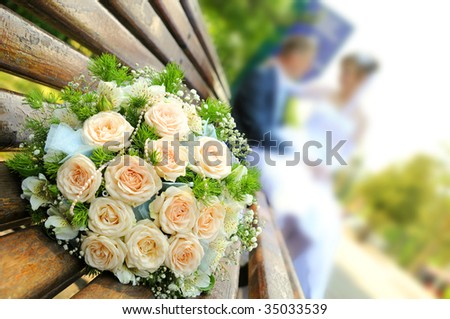 The beautiful wedding bouquet flowers lays on a bench, on a background a newly-married couple sit... Focus on a bouquet.