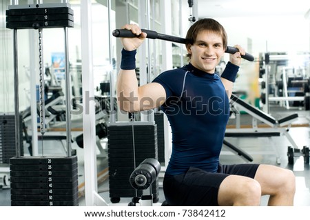 happy cutie athletic guy ,  execute exercise on sport-apparatus, in  sport-hall, look on camera and smile