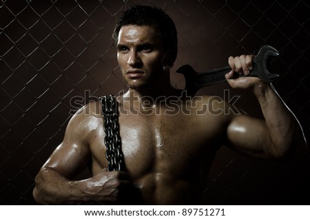 the beauty muscular worker  man,  with big wrench and  chain in hands, on netting fence background