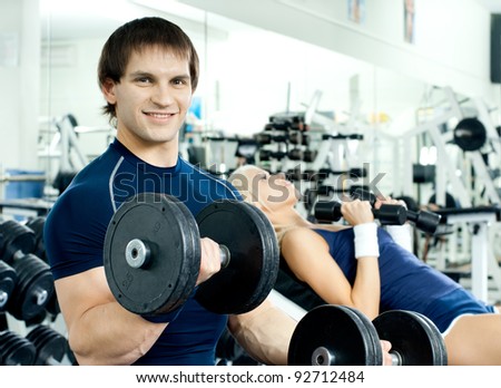 happy cutie athletic girl and guy,  exercise with dumbbells, look on camera and smile, in  sport-hall,