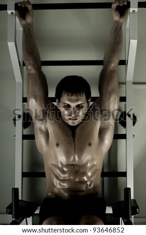 very power athletic guy ,  execute exercise tightening  on horizontal bar, in  sport-hall, hard light