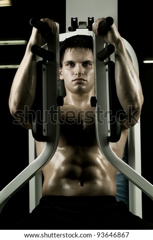 very power athletic guy ,  execute exercise on  on sport-apparatus, in  sport-hall, hard  light
