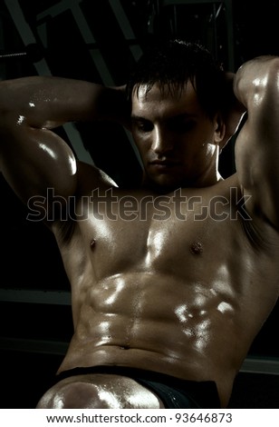 very power athletic guy ,  execute exercise on muscles belly, in  dark sport-hall