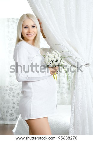 young pregnant woman with flowers, in white bedroom