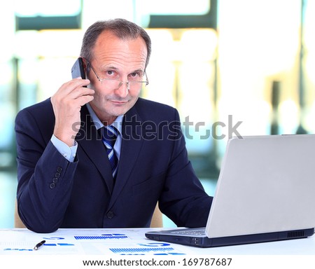 Portrait of smiling business man talking on cell phone and working on a laptop at office