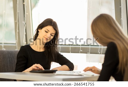 Young women working in the office, sitting at a table, using a calculator, smiling, colleagues