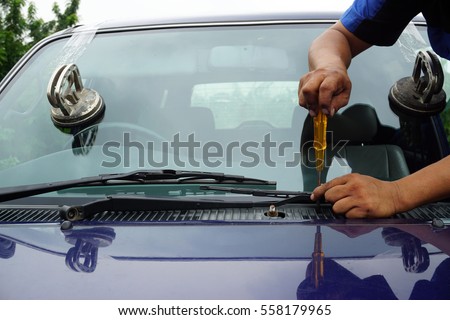 Glazier using tools repairing to fix crack broken windshield on the front window glass of the machine car accident.