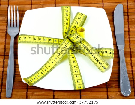 Ceramic plate with fork with knife and measuring tape. Symbolize a diet and the control over meal.