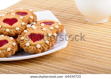 Cookies with a stuffing from red fruit jelly in the form of heart lay on the white plate and cup of tea in the background scene. Sweet valentine. Closeup.
