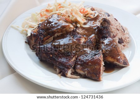 Caribbean style jerk chicken served with rice mixed with red kidney beans. Dish accompanied with coleslaw. Shallow Focus on the chicken.