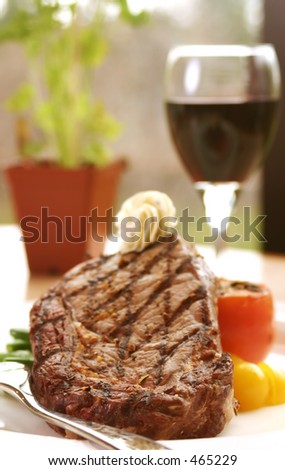 12oz ribeye steak topped with truffle butter and grilled tomato. Served with red wine. Shallow DOF.