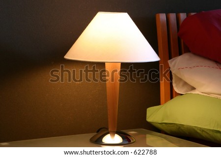 Shot of a bedside lamp against a backdrop of stacked pillows. Nice, warm late night tone to the image. Shallow DOF with focus on the lampshade.