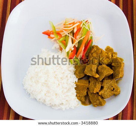 Caribbean style curried goat served with steamed rice. Dish accompanied with vegetable salad. Shallow DOF.