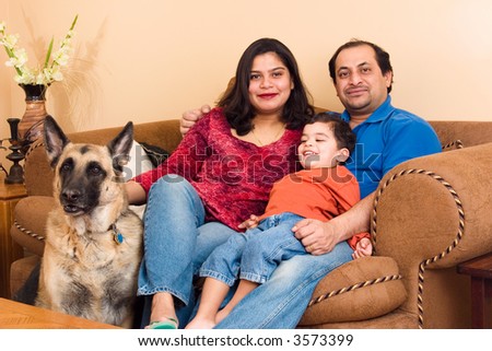 An East-Indian couple site in their living room with their son and dog