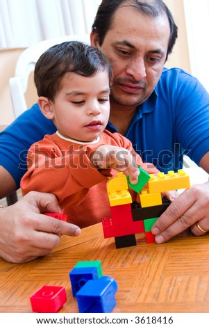 A father plays with his son and helps him build with his blocks