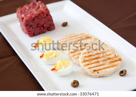 Exotic entree of bison tartare, herbed potato bread, deviled quail\'s eggs, fried ox-eyed capers and chervil essence
