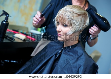 hair stylist using dryer on woman wet hair in salon