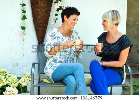 two woman friends chatting outdoors over coffee