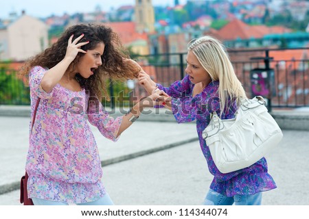 two woman fight each other in the street and pulling hair