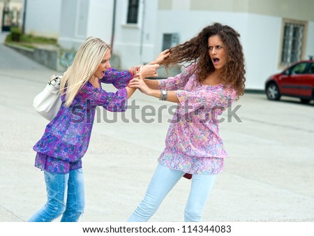 two woman fight each other in the street and pulling hair