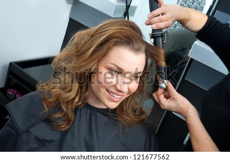 attractive woman in  hairsalon making new hairstyle with hair curler