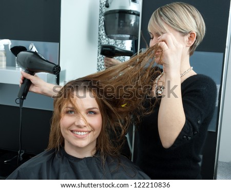 hair stylist drying woman hair with hair dryer in salon