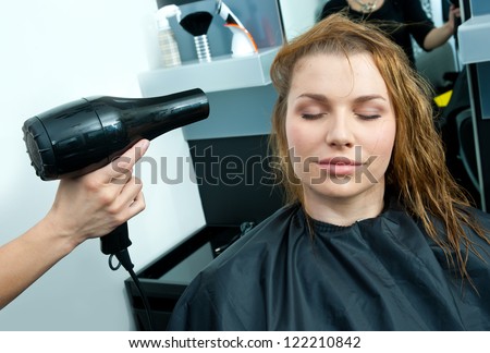 woman drying her wet hair with dryer in salon