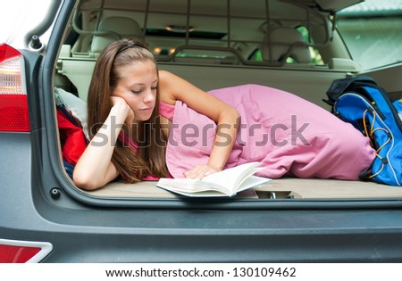 attractive adult woman reading book in trunk of her car